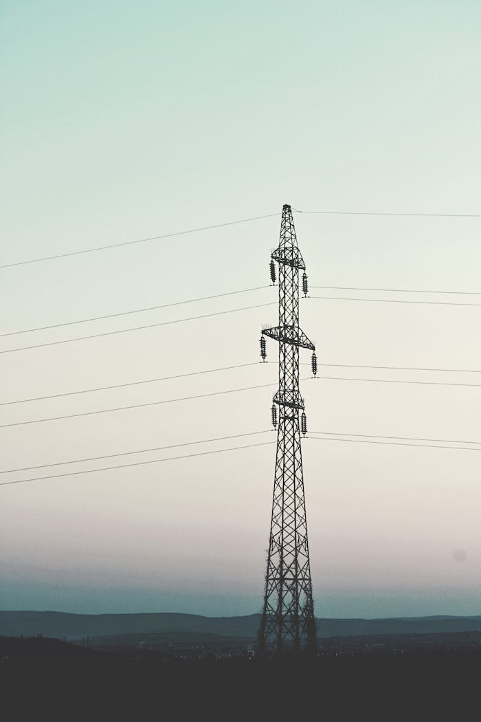 A tall transmission tower silhouetted against the clear sky during twilight, exhibiting power distribution infrastructure.